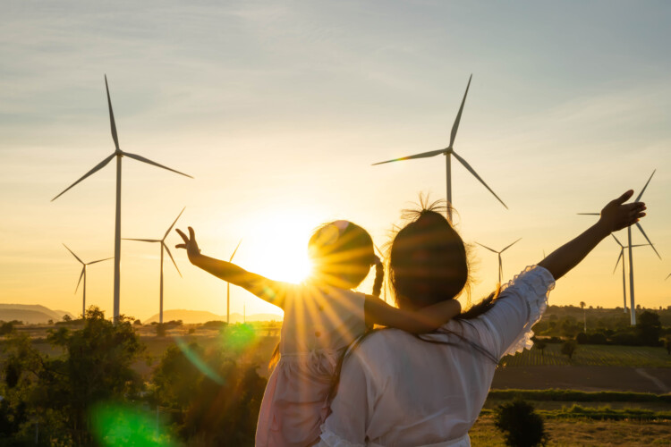 mother and child standing next to wind turbines at sunset