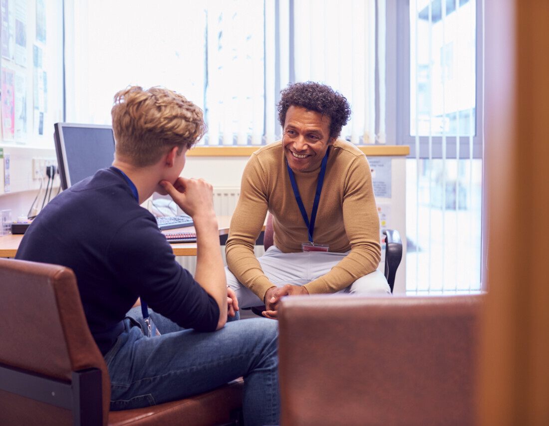 Male College Student Meeting With Campus Counselor Discussing Mental Health Issues